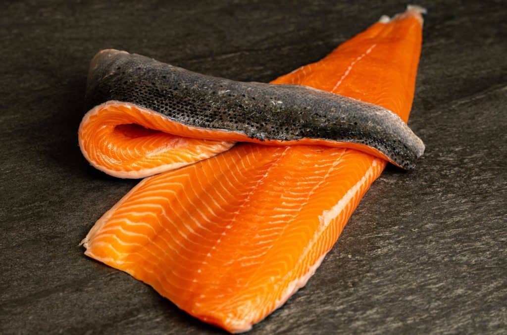 Fresh salmon fillets on dark surface.